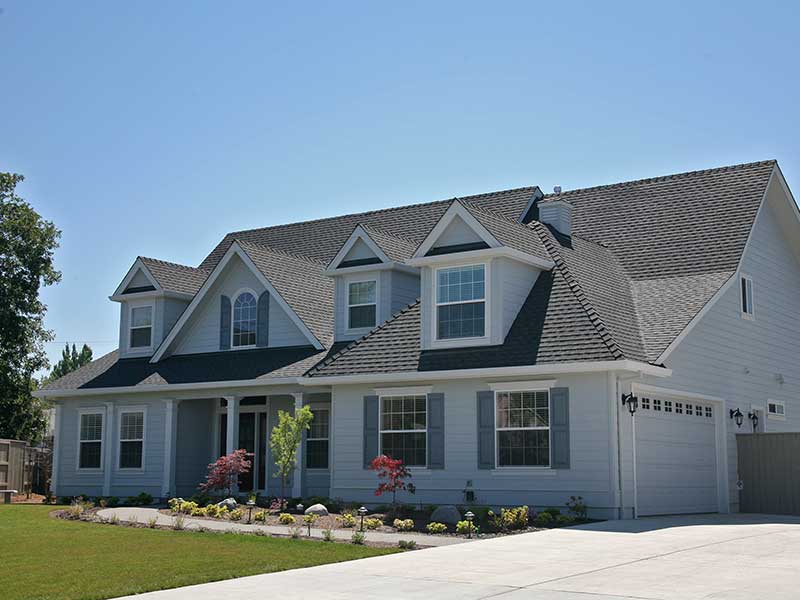 Two-story American home with gray shingles on its roof and light blue-ish siding